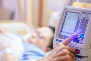 fingers press control panel for adjust Infusion pumps with blurry patient in hospital.